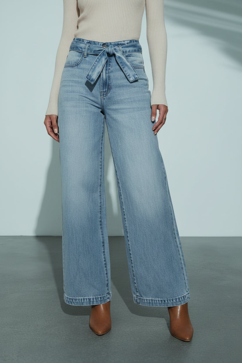 Person wearing light blue wide-leg jeans with a belt against a neutral background