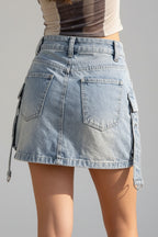 A person standing on a sandy beach wearing a light-wash denim cargo mini skirt with side ties and back pockets, paired with a striped crop top.