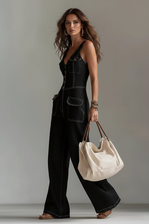 Woman wearing a black denim jumpsuit holding a beige handbag against a plain background
