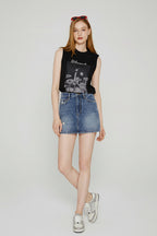 Woman wearing a black sleeveless top with graphic design and denim shorts on a white background