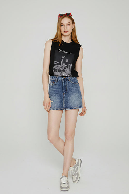 Woman wearing a black sleeveless top with graphic design and denim shorts on a white background