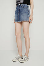 Person wearing a blue denim skirt and gray sneakers on a floral rug.