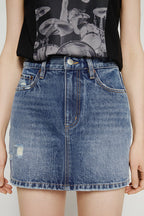 Person wearing a black graphic t-shirt and blue denim skirt on a plain background