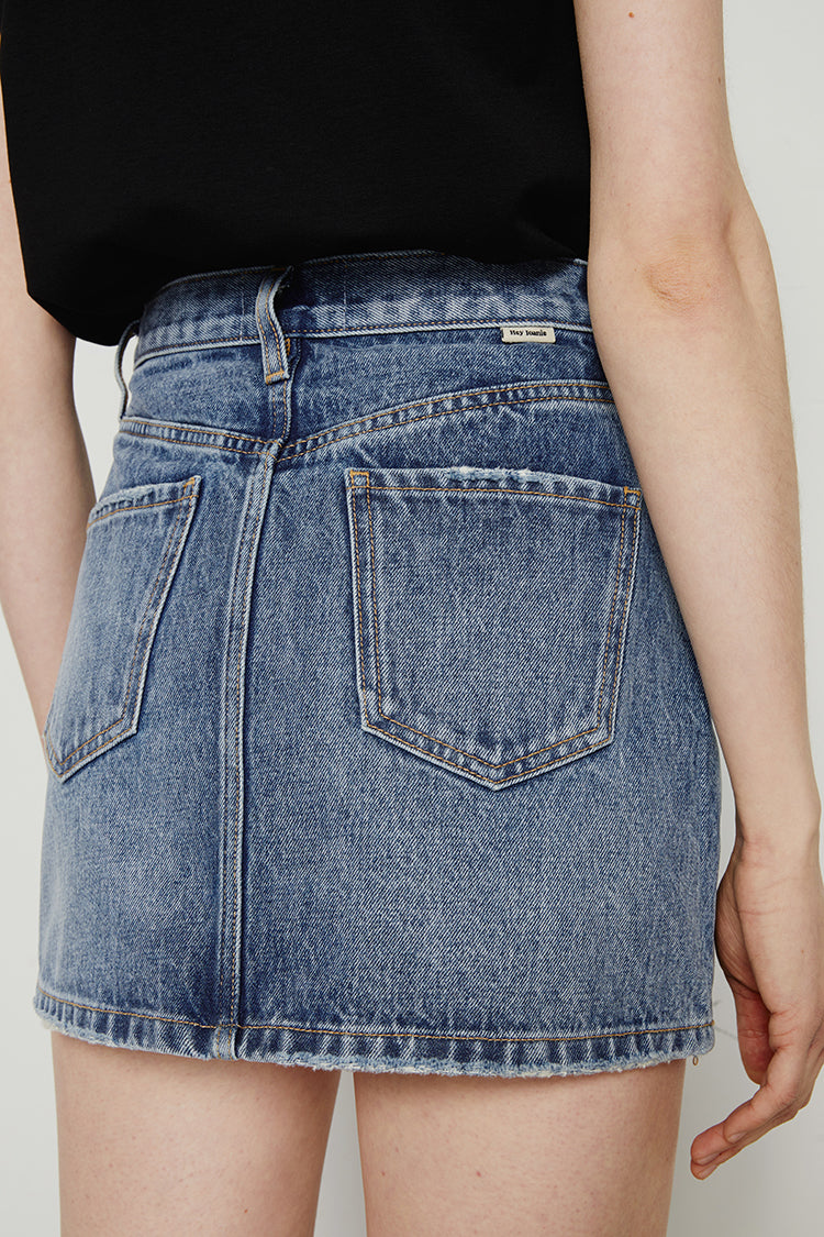 Person wearing a blue denim skirt with a plain background