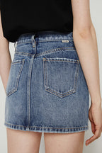Person wearing a blue denim skirt with a plain background