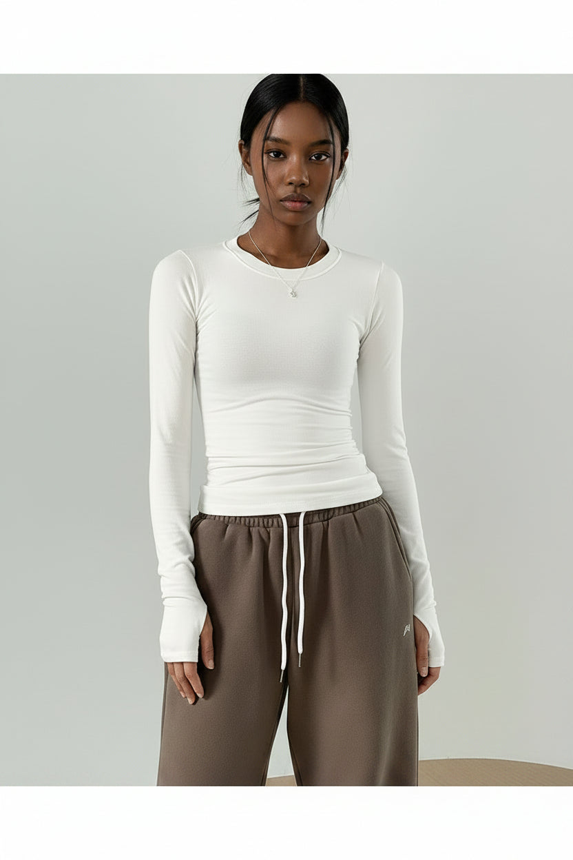 Person wearing a white long-sleeve top and brown pants against a plain background