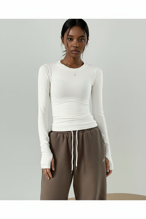 Person wearing a white long-sleeve top and brown pants against a plain background