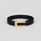 A black faux leather fashion belt with a gold rectangular metal buckle, displayed on a light beige background with sizing information and a width measurement of 2.5 cm.