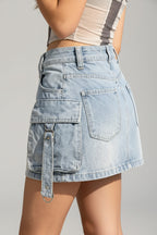 A person standing on a sandy beach wearing a light-wash denim mini skirt with large cargo pockets and a tie detail, paired with a striped crop top.