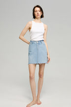 Woman wearing a white sleeveless top and light blue denim skirt on a gray background