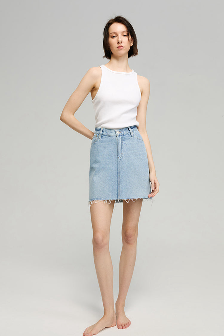 Woman wearing a white sleeveless top and light blue denim skirt on a gray background