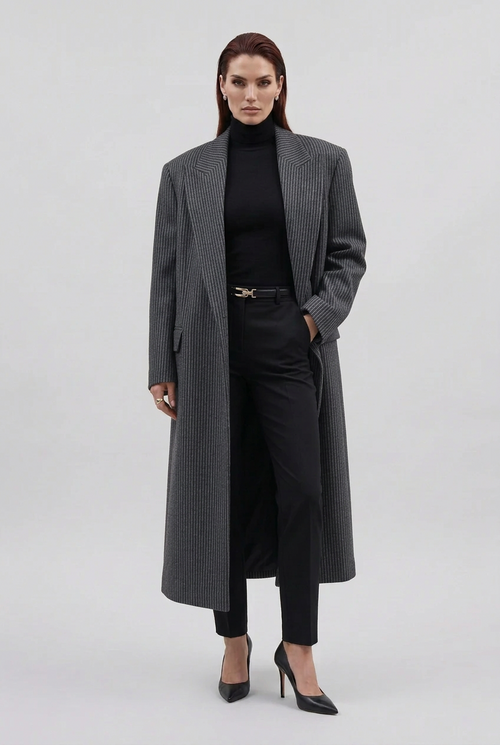 Person wearing a long dark coat and holding a brown leather bag, standing in front of a black vehicle.