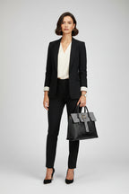 Black handbag with silver embellishments held by a person wearing a beige coat.