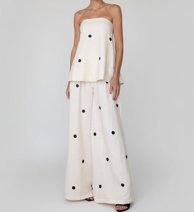 Woman wearing a white outfit with black polka dots in a bedroom setting.