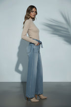 Woman wearing a beige top and light blue jeans against a plain background