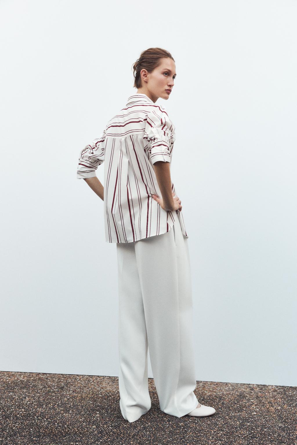 Woman wearing a striped shirt and white pants against a plain background