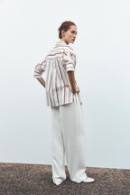 Woman wearing a striped shirt and white pants against a plain background