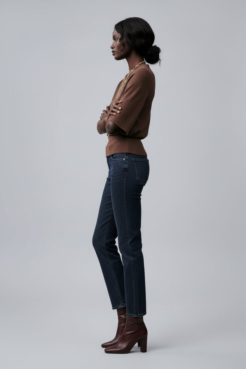Person wearing a brown sweater and dark jeans with a blurred background