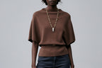 Woman wearing a brown sweater and dark blue jeans on a gray background