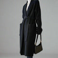 A model wearing a black, thick knitted windbreaker cardigan coat with long sleeves and a lapel collar, also carrying a black purse.