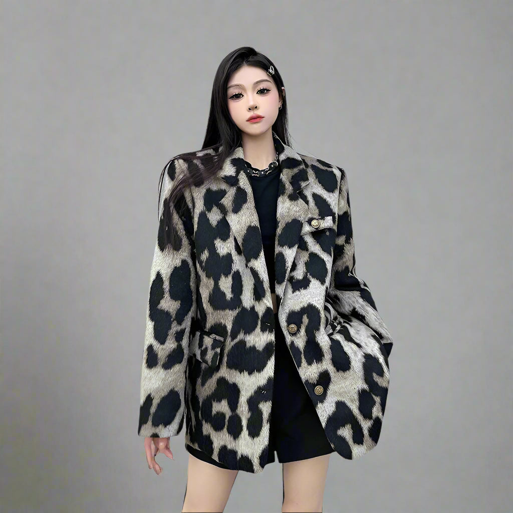 Woman wearing a leopard print coat standing against a gray wall.
