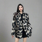 Woman wearing a leopard print coat standing against a gray wall.