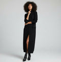 A woman wearing a long black cashmere cardigan coat with a quilted pattern, paired with black pants and a black belt.
