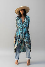 Woman wearing a tie-dye dress and straw hat against a gray wall