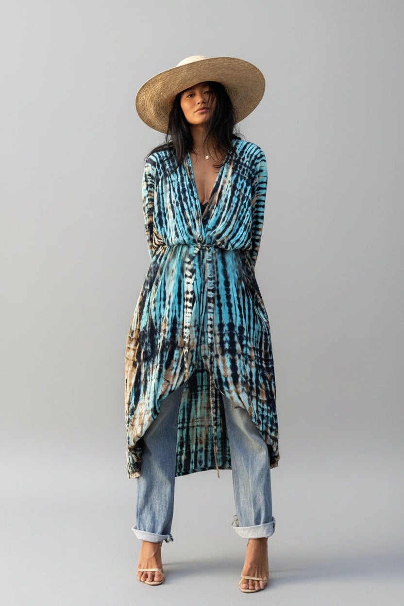 Woman wearing a tie-dye dress and straw hat against a gray wall
