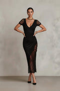 Woman wearing a black dress with lace details against a plain background