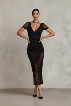 Woman wearing a black dress with lace details against a plain background
