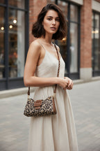 Person holding a leopard print handbag with a brown strap on an asphalt surface