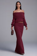 Woman wearing a burgundy off-shoulder top and skirt set against a neutral background