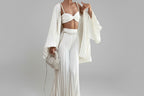 Woman in a white outfit with pearl accessories in a room.