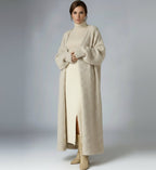 Person wearing a long beige coat over a white dress on a plain background