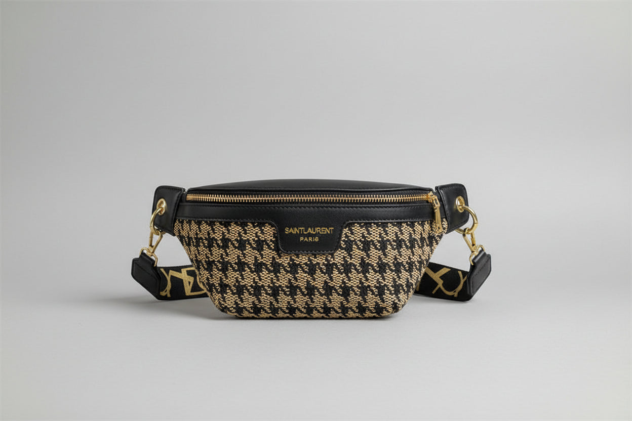 A black and brown houndstooth saddle bag with a zipper closure, a chain shoulder strap, and a soft carry handle.
