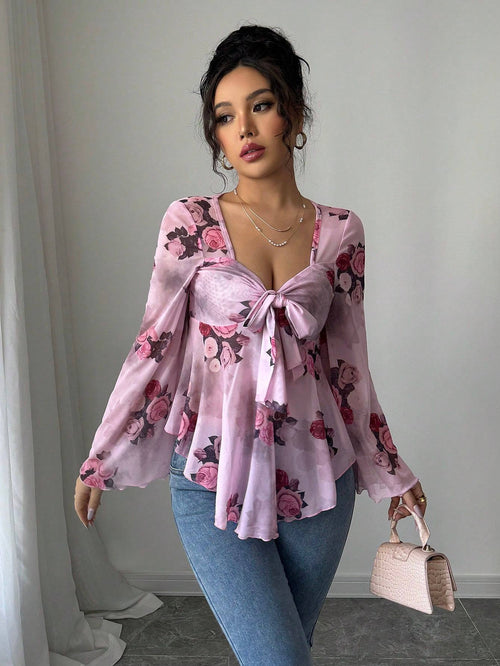 Woman wearing a pink floral blouse and blue jeans, holding a small handbag.