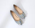 Flat shoes with gold buckles worn with light blue jeans on a white background