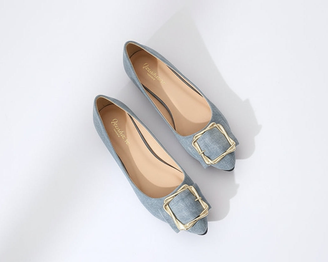 Flat shoes with gold buckles worn with light blue jeans on a white background