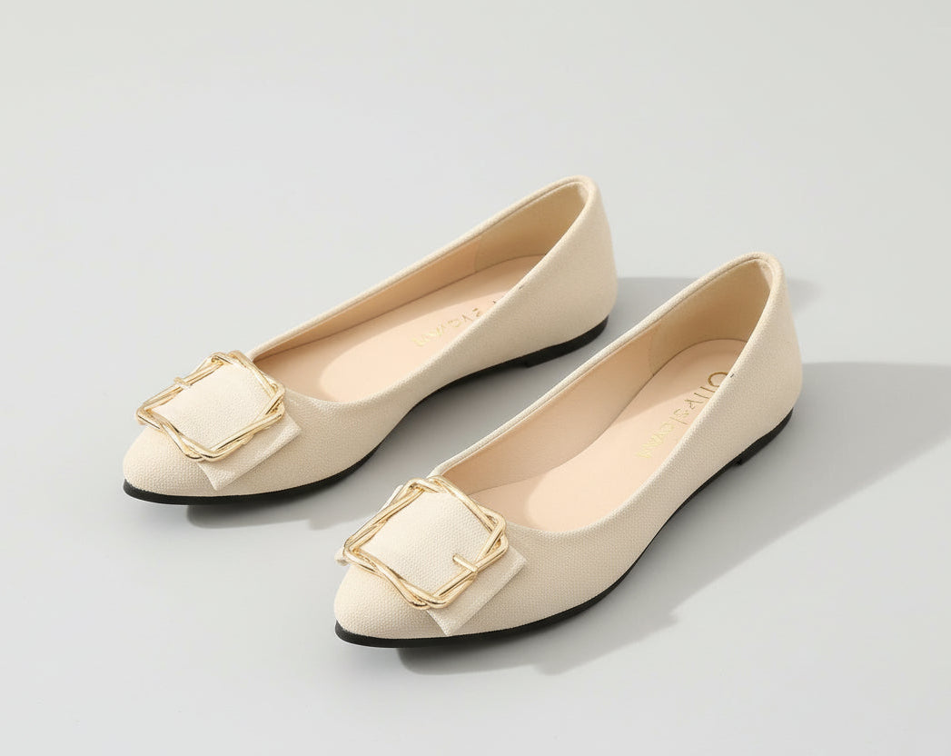 Pair of beige flat shoes with gold buckles on a light gray background