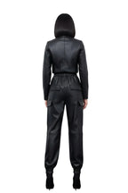 Person wearing a black leather jumpsuit against a white curtain background