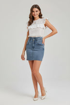 Woman wearing a white blouse with ruffled details and a denim skirt on a plain background