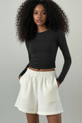 Person wearing a black long-sleeve crop top and white pants against a plain background