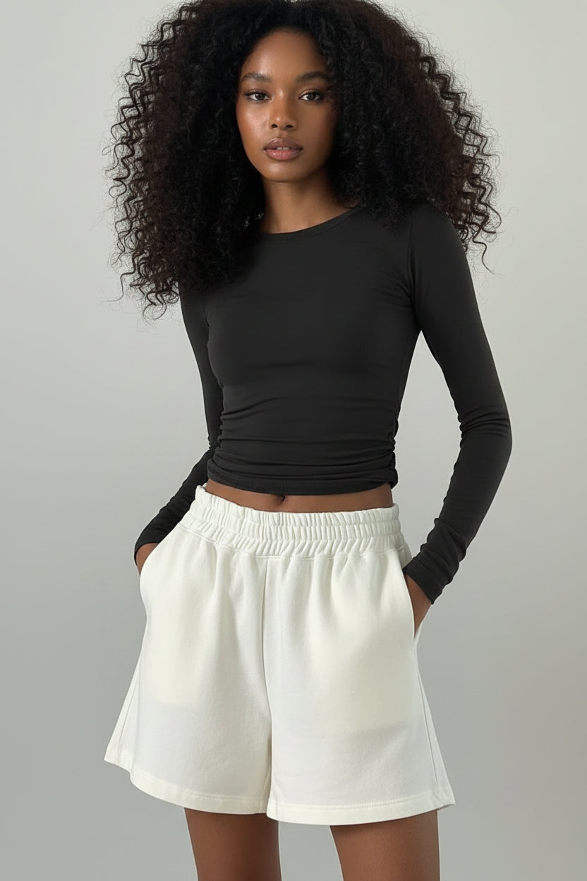 Person wearing a black long-sleeve crop top and white pants against a plain background