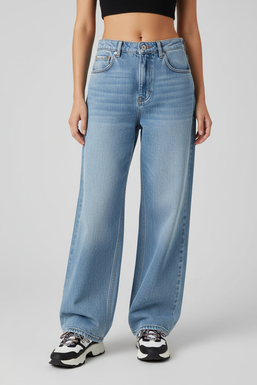 A model wearing light blue wide-leg denim jeans with a high waist, paired with black and white sneakers, shown from the waist down on a light gray studio background.