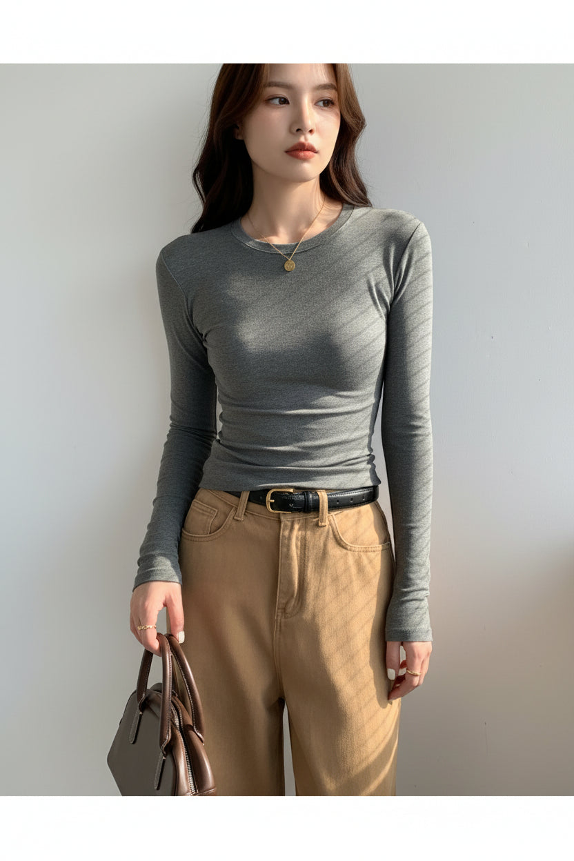 Person wearing a gray long-sleeve top and beige pants, holding a brown handbag against a light background.