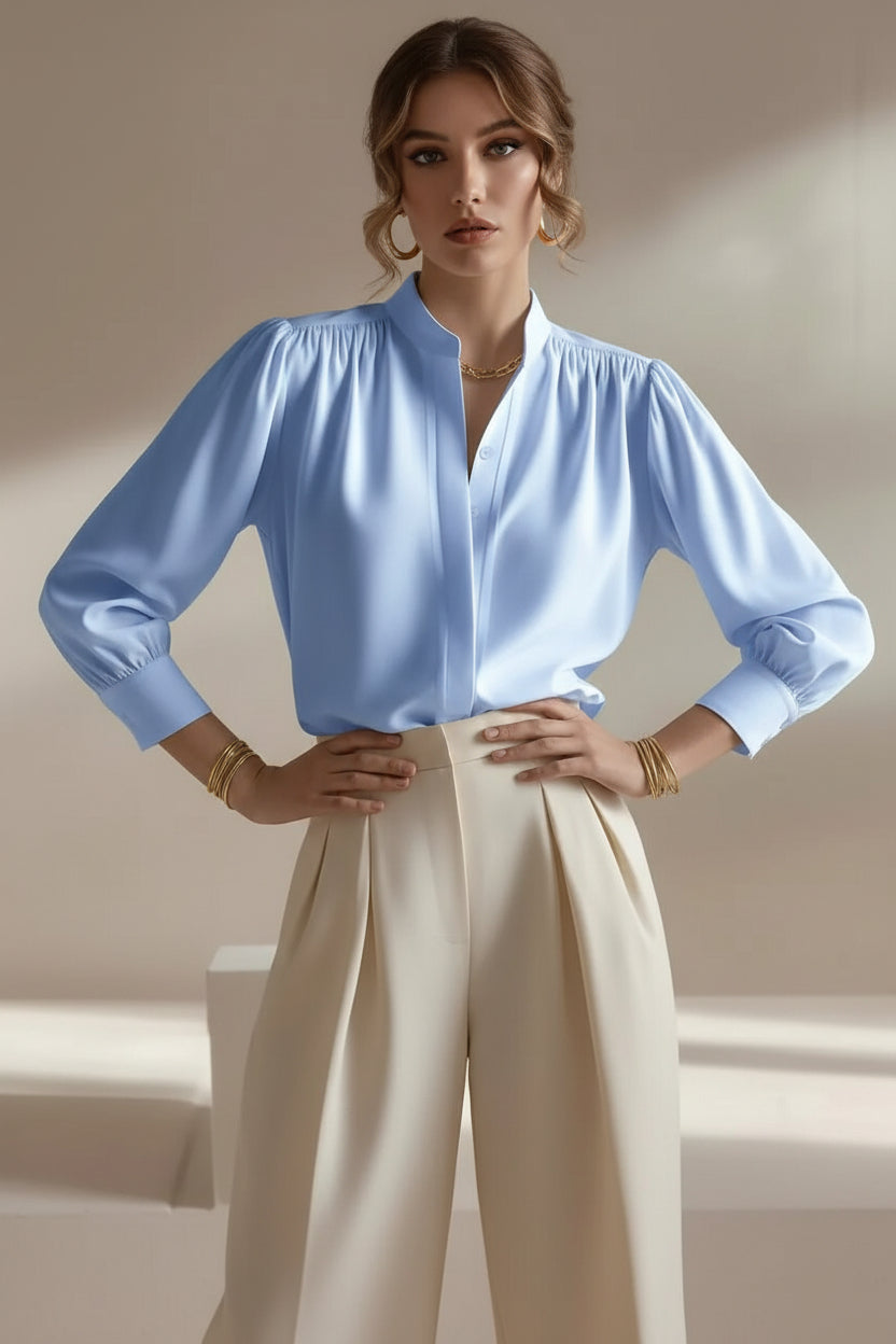 Woman wearing a light blue blouse with long sleeves and beige pants against a neutral background