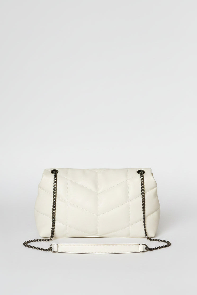 White handbag with chain strap held by a hand against a plain background