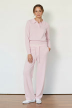 Woman wearing a pink outfit standing against a white wall.
