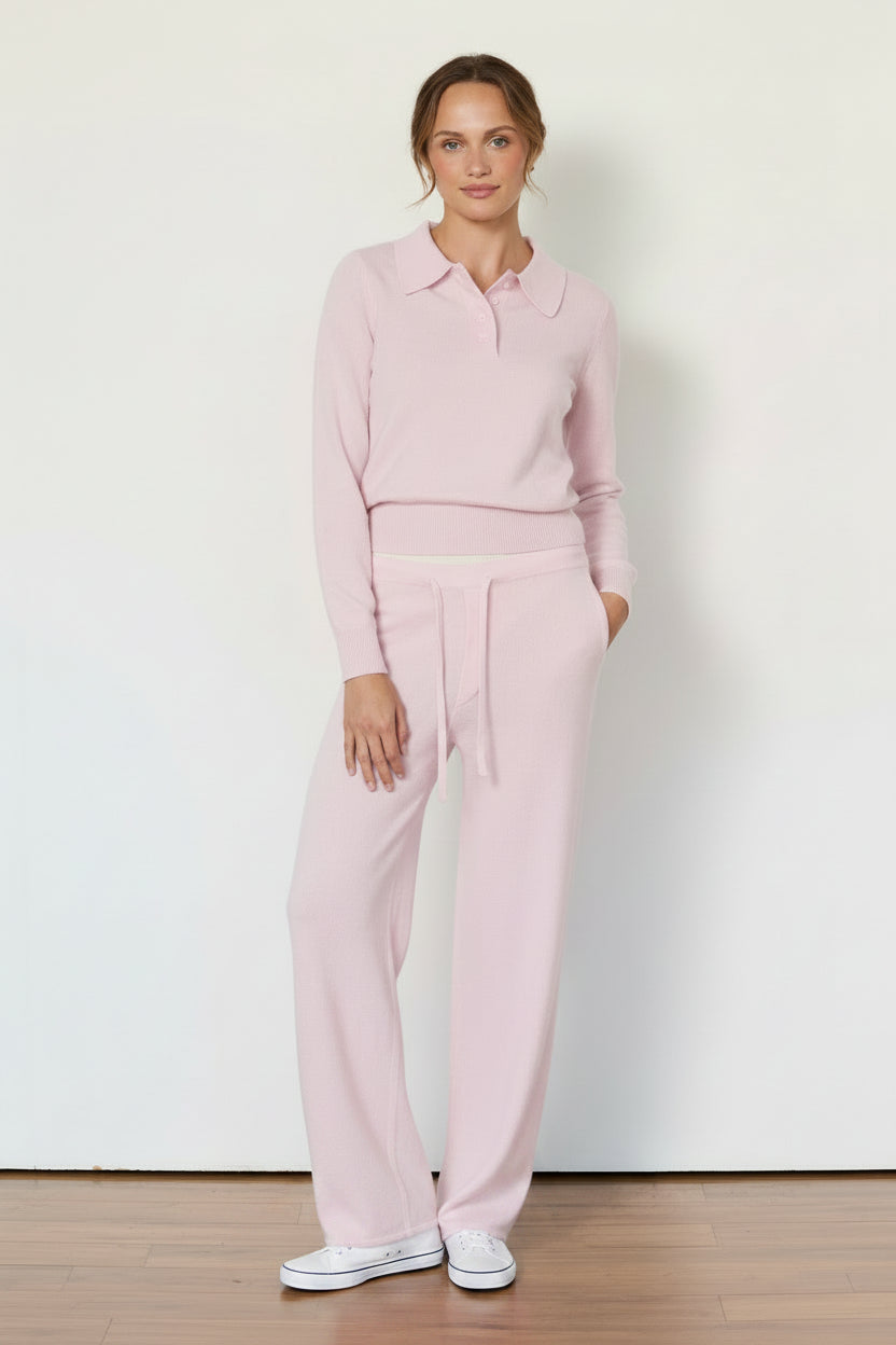 Woman wearing a pink outfit standing against a white wall.